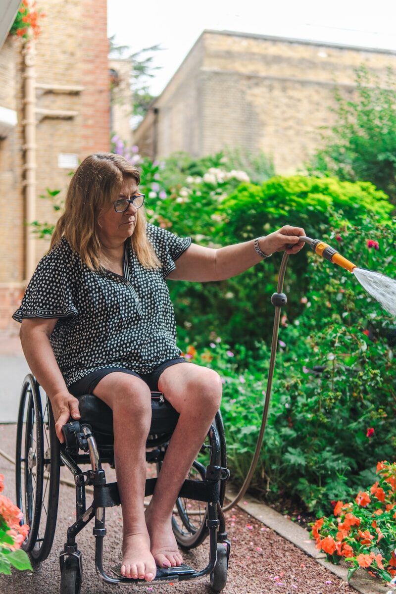 Woman in wheelchair watering plants in garden.